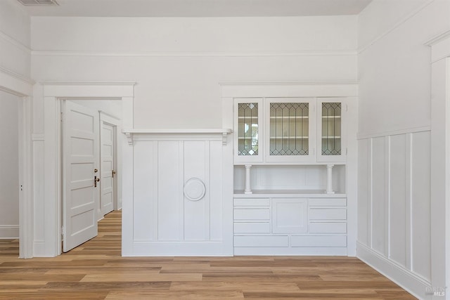 interior details featuring a decorative wall, wood finished floors, visible vents, and wainscoting