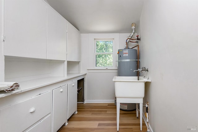 laundry room featuring a sink, baseboards, secured water heater, and light wood finished floors