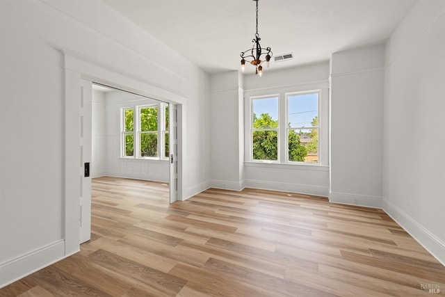 unfurnished dining area with a notable chandelier and light wood-type flooring