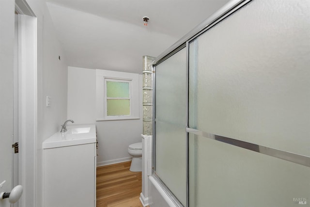 full bathroom with a shower with shower door, toilet, wood finished floors, baseboards, and vanity