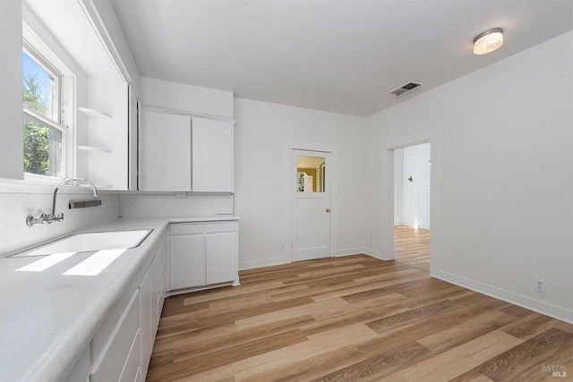 interior space with visible vents, a sink, light countertops, white cabinets, and light wood-style floors