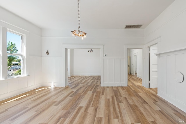 unfurnished dining area featuring visible vents, light wood-type flooring, wainscoting, an inviting chandelier, and a decorative wall