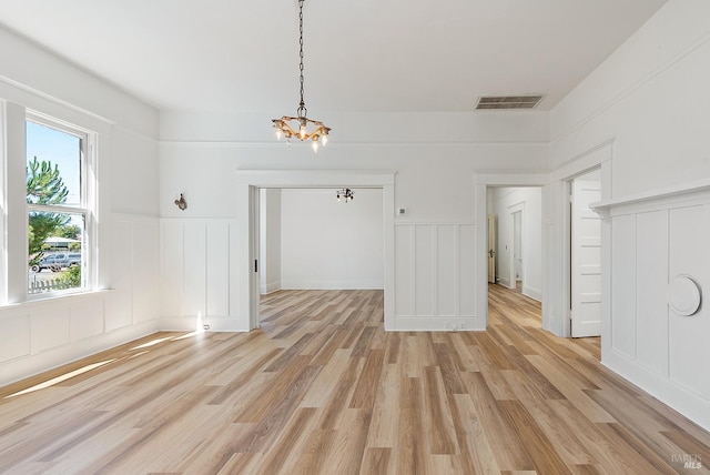 unfurnished dining area with light wood-type flooring, visible vents, a chandelier, and a decorative wall