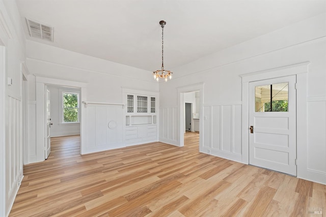 unfurnished dining area featuring a decorative wall, a notable chandelier, light wood-style floors, and visible vents