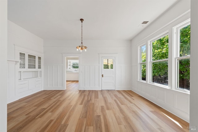 interior space with visible vents, a wainscoted wall, a notable chandelier, light wood-style flooring, and a decorative wall