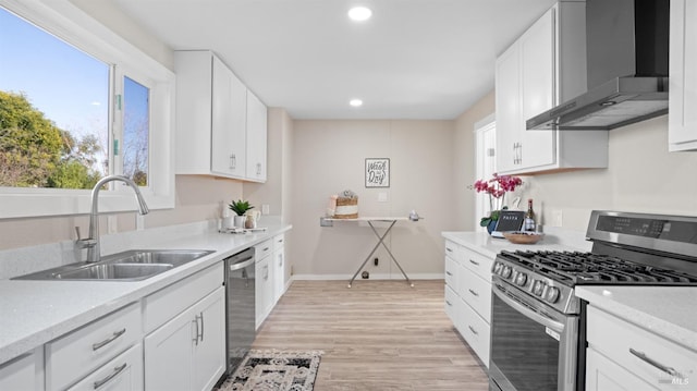 kitchen with wall chimney exhaust hood, white cabinetry, stainless steel appliances, and sink