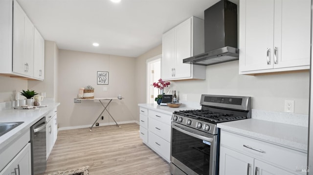 kitchen with white cabinetry, wall chimney range hood, light hardwood / wood-style floors, and appliances with stainless steel finishes