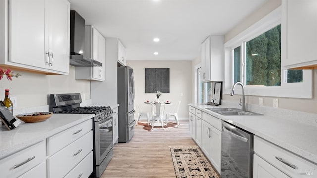 kitchen with appliances with stainless steel finishes, white cabinetry, sink, wall chimney range hood, and light wood-type flooring