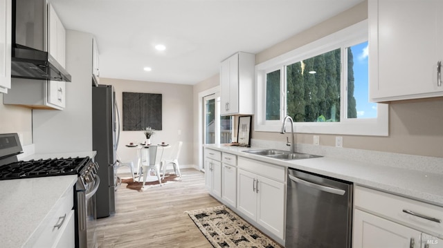 kitchen with white cabinetry, sink, light hardwood / wood-style flooring, stainless steel appliances, and wall chimney exhaust hood