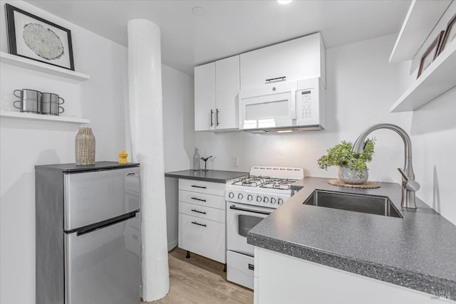 kitchen featuring white appliances, dark countertops, a sink, and white cabinets