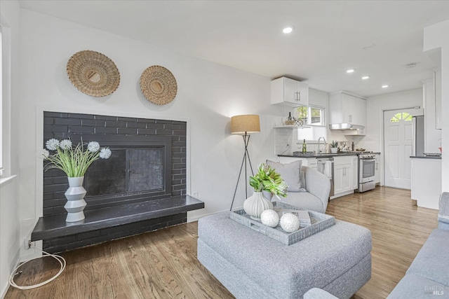 living room featuring light wood finished floors, a glass covered fireplace, and recessed lighting