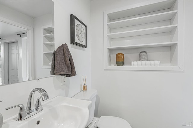 bathroom featuring toilet, built in shelves, and a sink