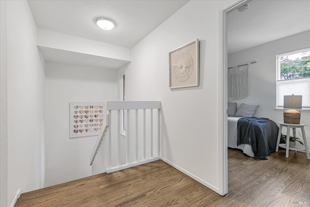 corridor featuring baseboards, an upstairs landing, and wood finished floors