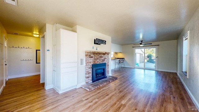 unfurnished living room featuring ceiling fan, hardwood / wood-style flooring, a fireplace, and a textured ceiling