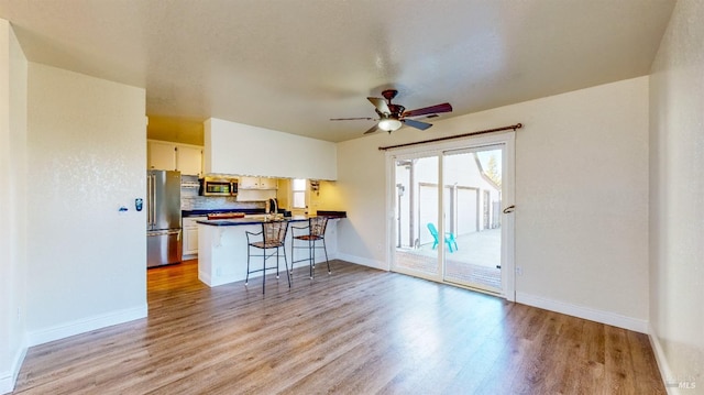 kitchen with light hardwood / wood-style flooring, a breakfast bar area, stainless steel appliances, white cabinets, and kitchen peninsula