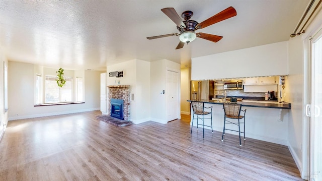 unfurnished living room featuring ceiling fan, light hardwood / wood-style floors, a brick fireplace, and a textured ceiling