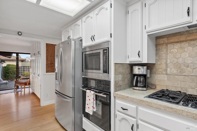 kitchen with backsplash, appliances with stainless steel finishes, light wood-type flooring, and white cabinets