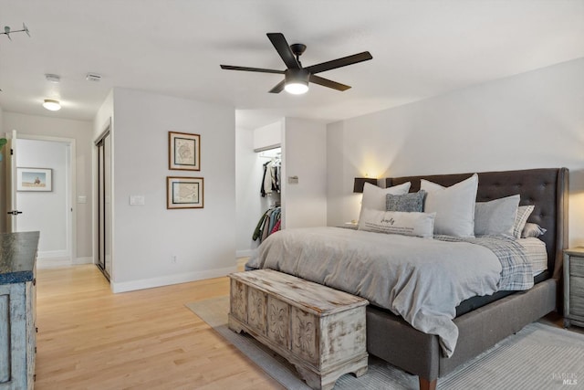 bedroom with a closet, a walk in closet, ceiling fan, and light hardwood / wood-style flooring