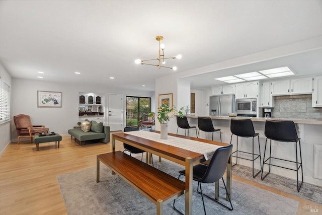 dining room with a skylight, an inviting chandelier, and light hardwood / wood-style flooring