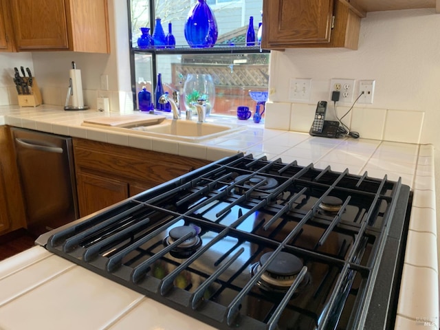 kitchen featuring stainless steel dishwasher, stovetop, tile counters, and sink