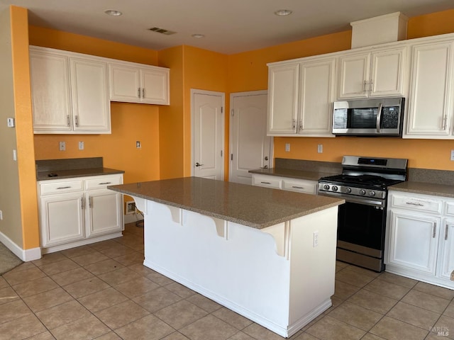 kitchen with a breakfast bar area, white cabinets, a center island, light tile patterned floors, and stainless steel appliances