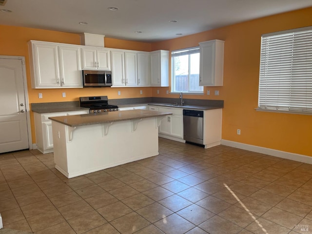 kitchen with light tile patterned floors, appliances with stainless steel finishes, white cabinetry, a kitchen breakfast bar, and a center island