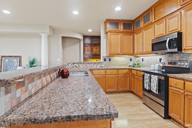 kitchen featuring stainless steel appliances, decorative backsplash, a sink, light stone countertops, and light wood-type flooring