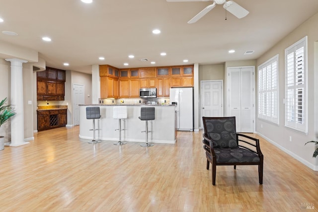 kitchen featuring a kitchen breakfast bar, light wood-style floors, freestanding refrigerator, stainless steel microwave, and decorative columns