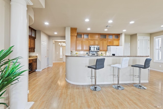 kitchen with light stone counters, a kitchen bar, white refrigerator with ice dispenser, and light hardwood / wood-style floors