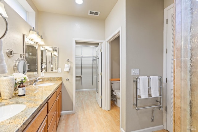 bathroom with double vanity, visible vents, toilet, a sink, and wood finished floors