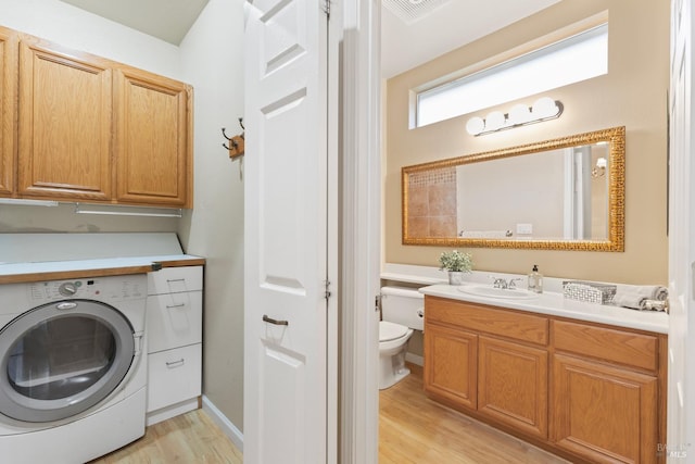 clothes washing area with light hardwood / wood-style floors, cabinets, washer / dryer, and sink