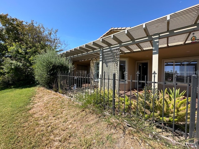 view of home's exterior featuring stucco siding, a lawn, fence, and a pergola