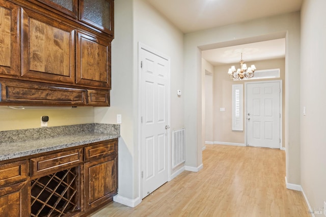 kitchen featuring light stone countertops, decorative light fixtures, an inviting chandelier, and light hardwood / wood-style flooring