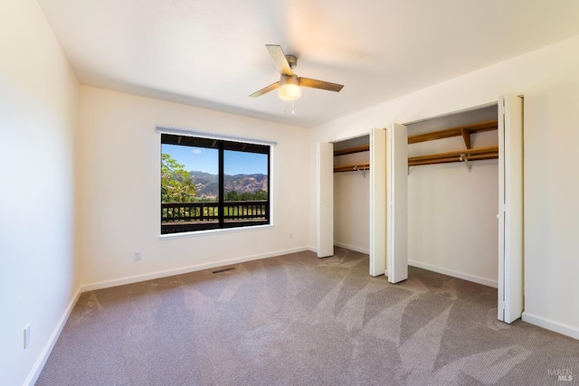 unfurnished bedroom featuring multiple closets, ceiling fan, and light carpet