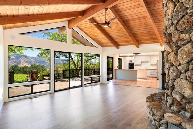 unfurnished living room featuring high vaulted ceiling, beamed ceiling, light hardwood / wood-style floors, a mountain view, and wooden ceiling