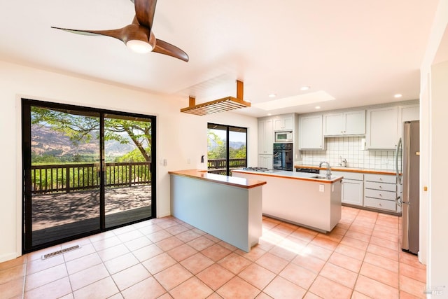 kitchen featuring a breakfast bar area, tasteful backsplash, stainless steel fridge, kitchen peninsula, and white cabinets