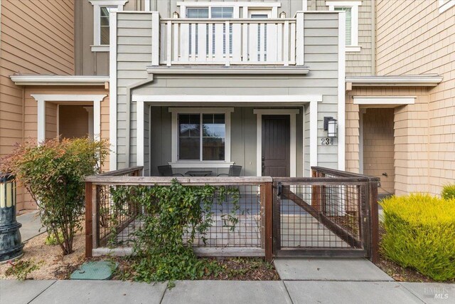 doorway to property with covered porch, a balcony, and a gate