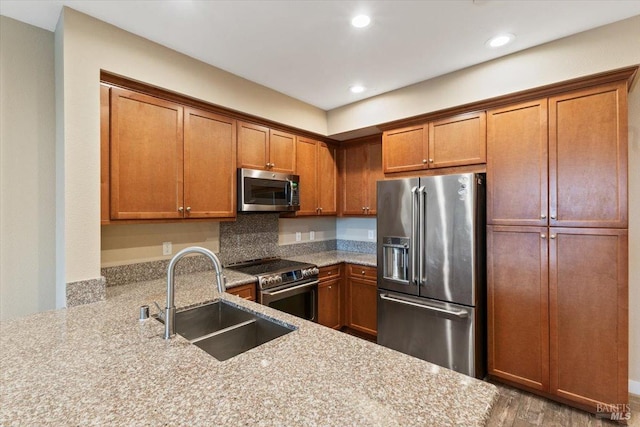 kitchen with a sink, brown cabinetry, stainless steel appliances, light stone countertops, and recessed lighting