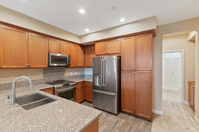 kitchen with brown cabinets, light stone counters, stainless steel appliances, and a sink