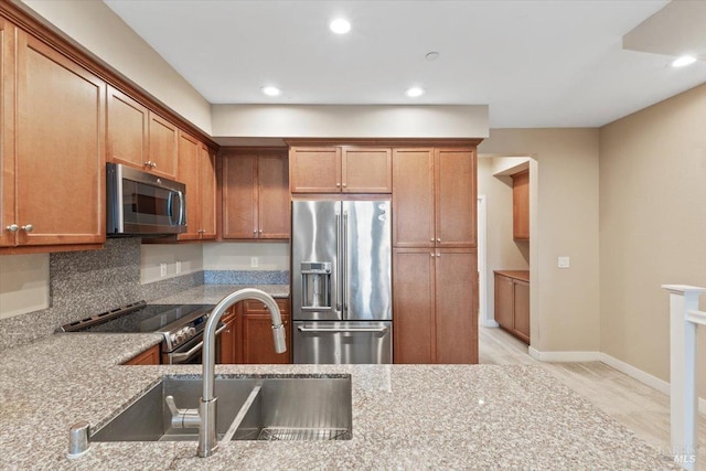 kitchen with light stone counters, a sink, brown cabinetry, stainless steel appliances, and recessed lighting