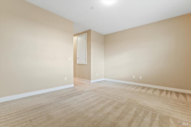 unfurnished room featuring light carpet and baseboards