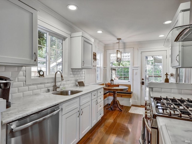 kitchen featuring white cabinets, light stone counters, stainless steel appliances, pendant lighting, and a sink