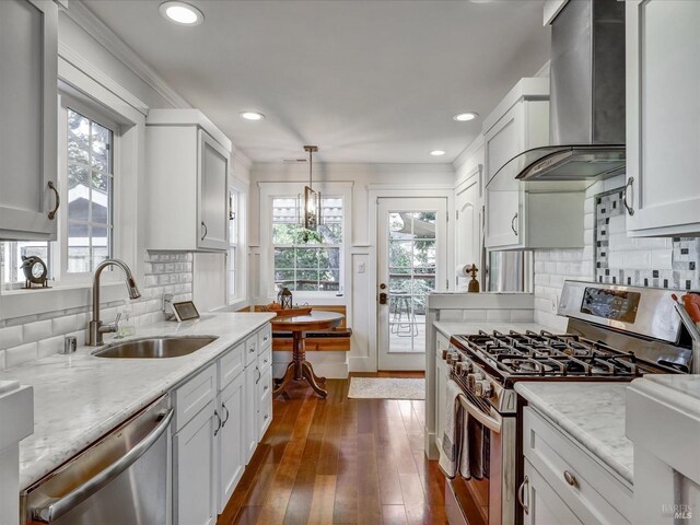 kitchen featuring sink, appliances with stainless steel finishes, white cabinetry, hanging light fixtures, and wall chimney exhaust hood