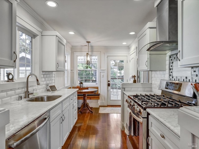 kitchen with white cabinets, wall chimney exhaust hood, appliances with stainless steel finishes, decorative light fixtures, and a sink