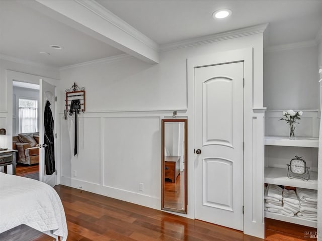 bedroom featuring ornamental molding, a decorative wall, dark wood-type flooring, and wainscoting