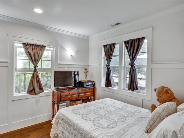 bedroom featuring visible vents, wainscoting, wood finished floors, crown molding, and a decorative wall