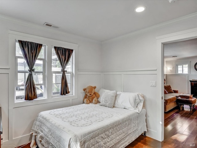 bedroom with dark wood-type flooring, visible vents, crown molding, and a decorative wall