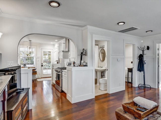 kitchen featuring light countertops, visible vents, stainless steel gas stove, white cabinetry, and wall chimney range hood