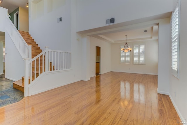 unfurnished living room with a tray ceiling, a chandelier, and light wood-type flooring