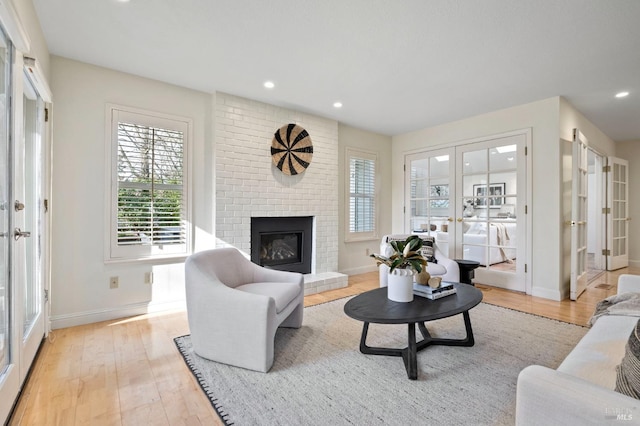 living room featuring french doors, a brick fireplace, and light hardwood / wood-style flooring